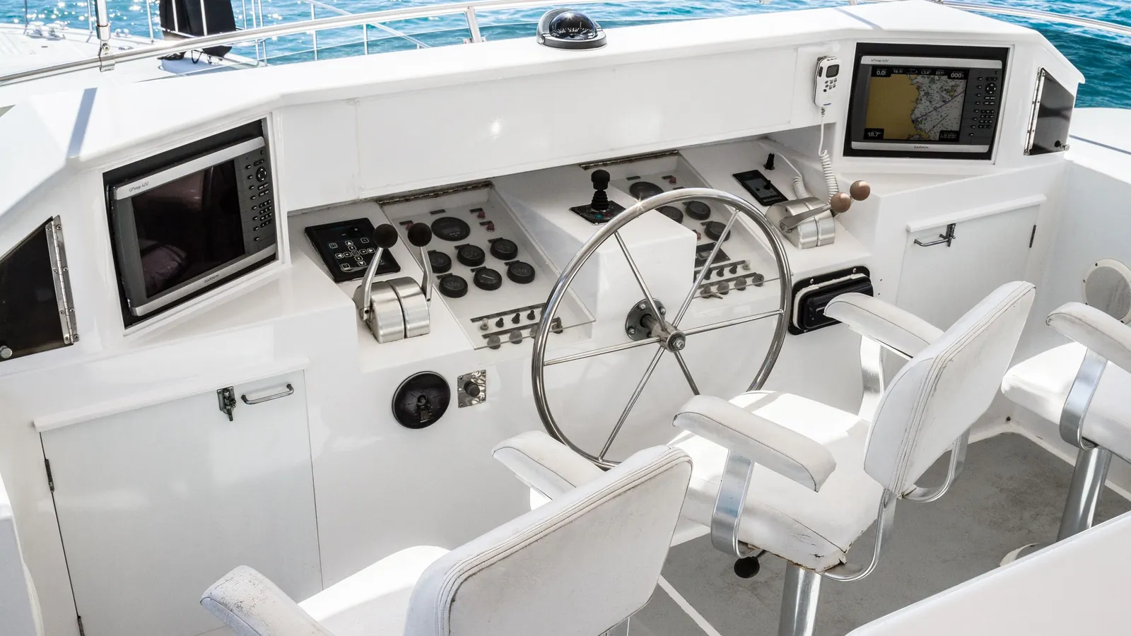 The helm of a motorboat with steering wheel, throttles, instruments and two chart plotters, the open sea behind.