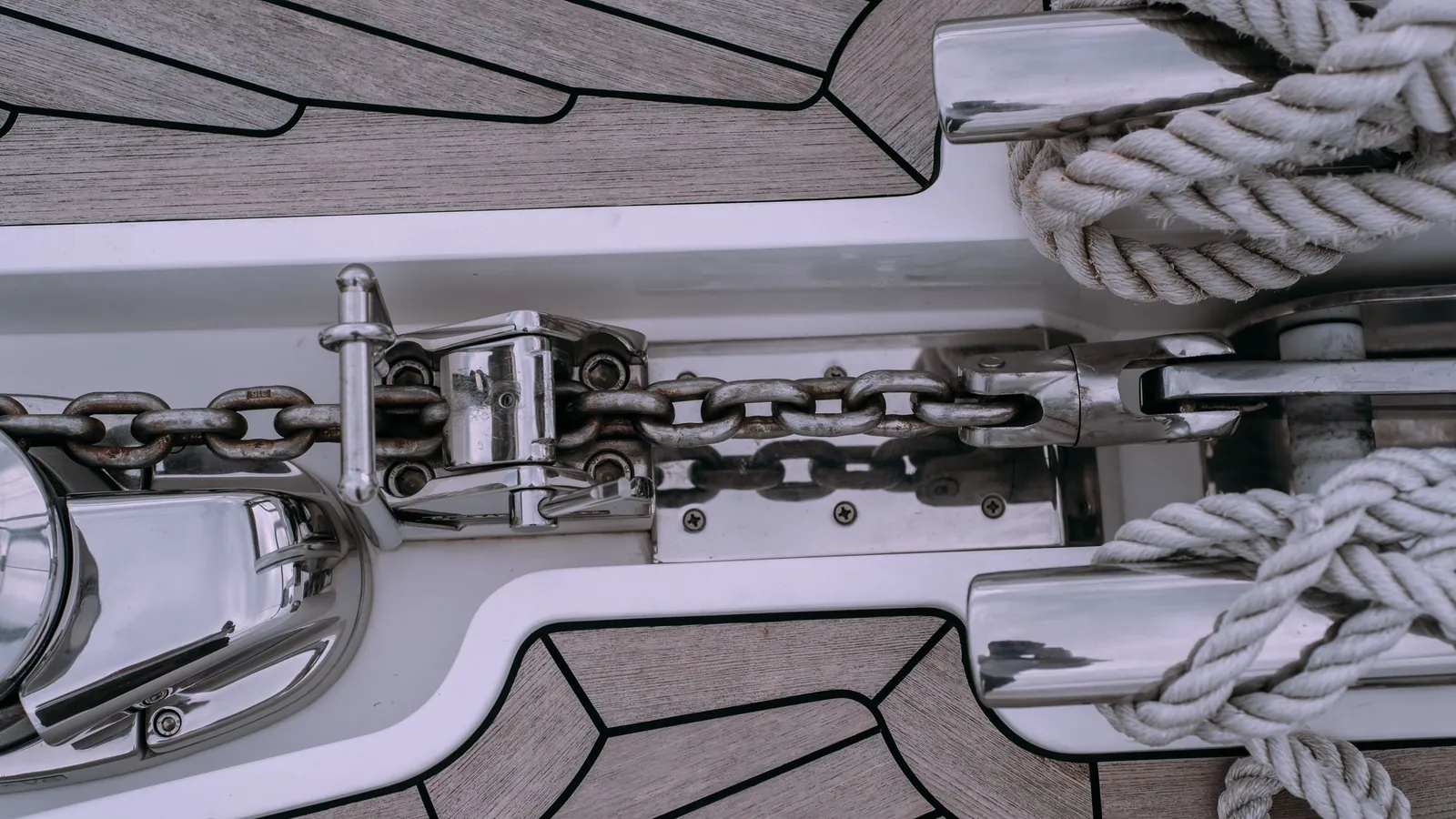 The foredeck of a yacht seen from above: the anchor chain runs from the windlass through the chain stopper to the anchor stowed in the bow fitting, with mooring lines made fast beside it.